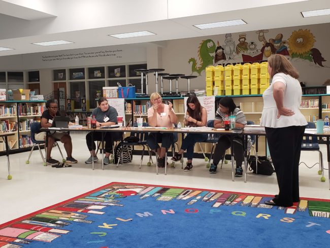 Teachers sitting at a long table in a school library.