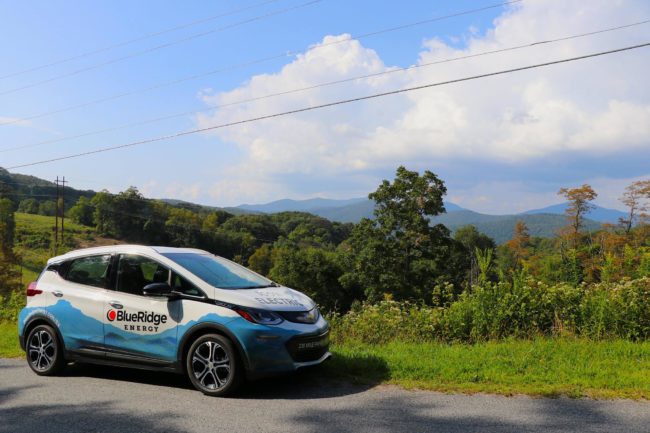 Electric vehicle with "Blue Ridge Energy" on the side parked in front of a scenic mountain view.
